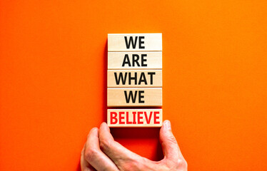 We are what we believe symbol. Concept words We are what we believe on wooden blocks. Businessman hand. Beautiful orange background. Business, motivational we are what we believe concept. Copy space.