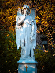statue of an angel in the cemetery with autumn leaves