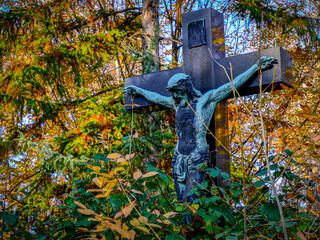Jesus on the cross among autumn leaves in cemetery