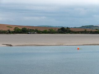 A orange buoy on a water surface. The sandy shore of the sea bay. The coastline on a cloudy day. Seaside landscape.