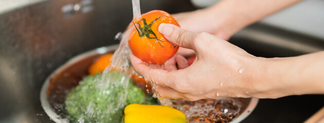 Close up asian young woman washing tomato, broccoli, carrot fresh vegetables, paprika with splash...