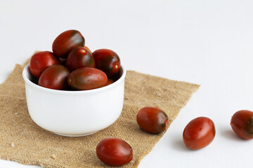 cherry tomatoes in the white bowl and sackcloth. Fresh red cherry tomatoes with water drops on white background. copy space.