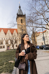 Tourist with paper cup walking on urban street and looking away in Prague.