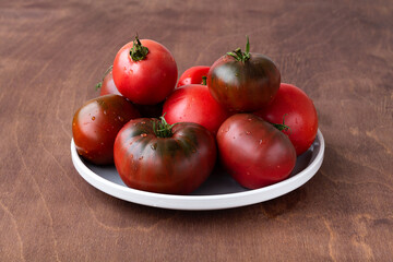 Fresh big raddish-purple tomatoes with water drops on wooden background. red tomatoes on the white plate on table. copy space