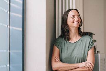 Businesswoman with arms crossed leaning against a wall in office and taking a break