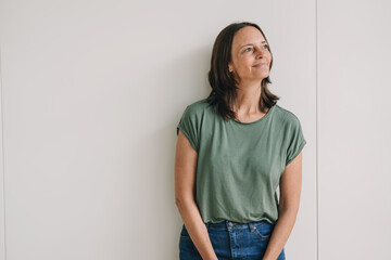 businesswoman with t-shirt leans against office wall and looks to the side