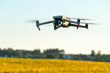 A modern quadcopter flies over a field of sunflowers against the sunset. The use of modern technologies in the agro-industrial complex. The drone helps the farmer in agribusiness.
