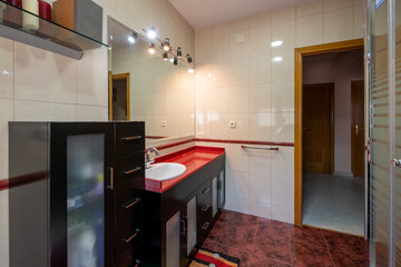Bathroom with white porcelain fixtures, red countertops over dark wood cabinets, and mirror sconces