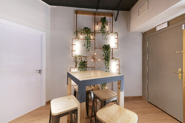 A restaurant room with tall wooden tables and chairs and a copper shelf with artificial plants