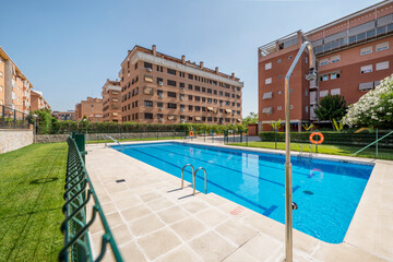 Swimming pool of an urbanization with metal stairs and gardens with grass and metal fence next to a...