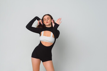 sexy brunette in a black dance bodysuit and a white top with long nails poses dances, shows her palm. Portrait of a beautiful young woman in the studio on a white background, copy space.