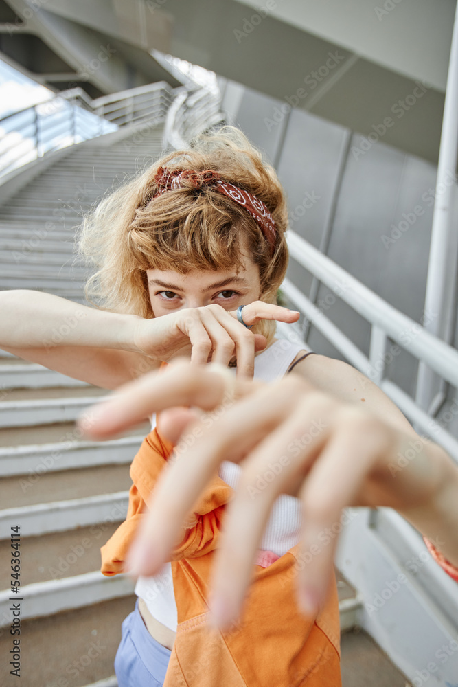 Wall mural Vertical portrait of young woman posing outdoors in urban setting and reaching out to camera