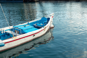 White fishing boat in the marine harbor. Blue plastic chair on the stern.
