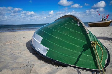 Green upside-down boat at the sandy beach with the sea in the background