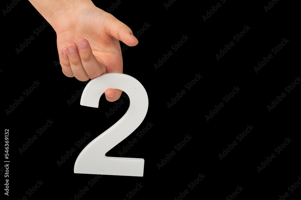 Poster close-up hand holding a white number 2 on a black background. number two isolate on black background