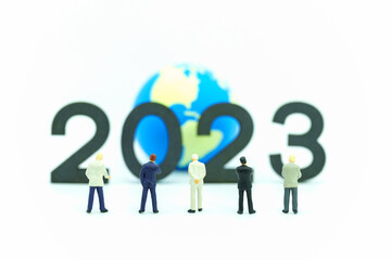 2023 Global Business New Year Concept. Closeup of group of businessman miniature figures standing and looking to number  and mini world ball on white background.