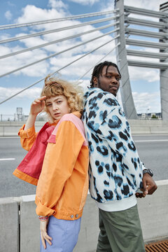 Vertical portrait of two young people wearing colorful clothes while posing on city bridge
