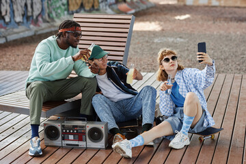 Diverse group of young people hanging out outdoors with boombox and taking selfie photos