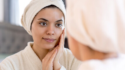 beauty, skin care and people concept - smiling young woman in skin care and looking to mirror at home bathroom