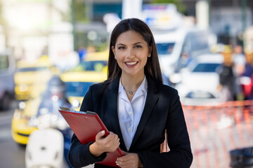Portrait of a young, professional woman in business clothing holding a filecase in the city center...