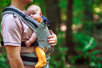 A young father walks with a baby in a sling backpack outside