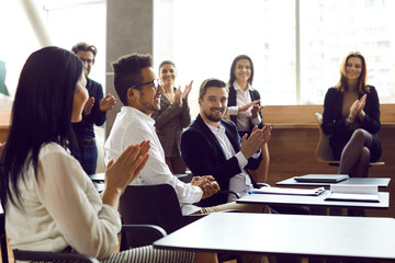 Business people applaud cheers man on business meeting or training in bright modern office. Colleagues congratulate man clapping hands on business achievements, excellent work results or promotion. - obrazy, fototapety, plakaty