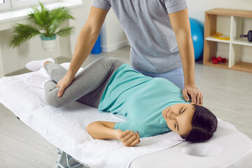 Professional physiotherapist or chiropractor does exercises to correct young woman's spine. Male...