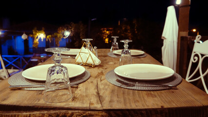 Empty table decorated with glasses, cutlery, dishes and placemats on the terrace on a summer evening. An empty decorated table ready to serve people.