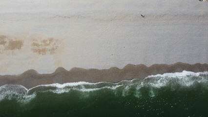 Aerial drone view of foamy waves crashing on a sandy beach on a sunny day