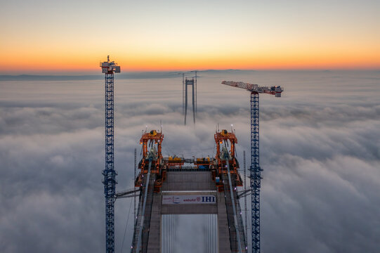 Braila, Romania - November 13, 2022: IHI Webuild japonese company building the bridge over Danube River near Braila City in Romania. Panoramic aerial drone view from above of the suspended bridge.