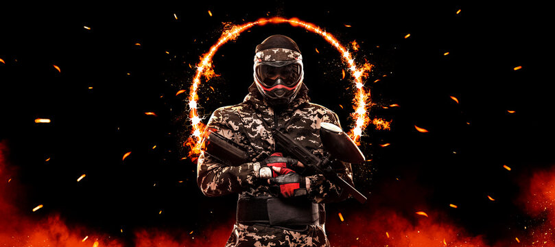 Paintball player man. Lasertag game. armed masked paint ball soldier on fire background. Advertisement design for paintball park.