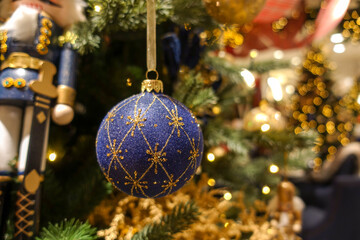 Blue Christmas ball bauble ornament with gold glitter details against out of focus christmas tree warm background and nutcracker