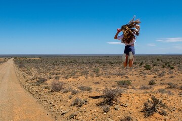Back view of female jumping over field with growing bushes in Africa