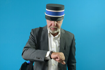 The train conductor carefully looks at his wristwatch before the train leaves. On a blue background