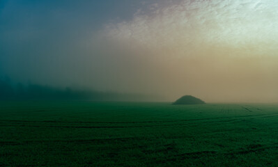 Naklejka na ściany i meble Background of an agricultural field with a pile in the middle of the field on a foggy day
