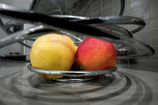 Red And Yellow Apples In Modern Steel Fruit Bowl Standing On Countertop At Home Close Up Low Angle View