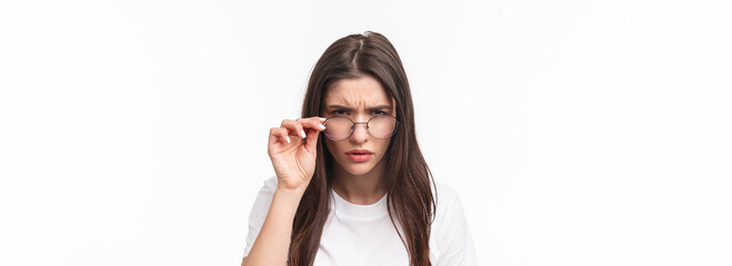 Close-up portrait of suspicious young serious-looking woman, look from under glasses, squinting at person with judgemental disbelief stare, standing white background, have doubts - obrazy, fototapety, plakaty