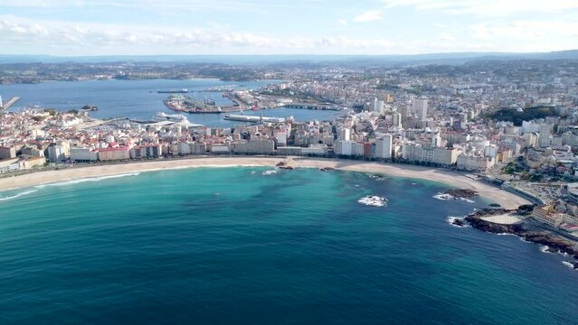 Drone point of view of Galician city A Coruna. View of famous beach Orzan. In background the city center and the harbour area. Drone backward Travel destination in Northwest of Spain 