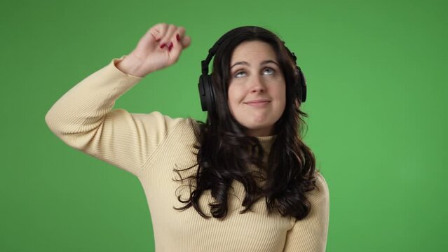Happy smiling young woman wearing headphones earphones dancing isolated on a green screen background.