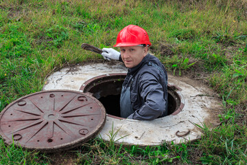 A male plumber in a helmet descended into an open water well for inspection and repair