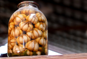 pickled garlic in a large glass jar on a wooden shelf. Tasty pickled garlic