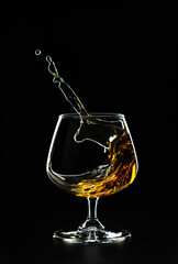 A splash of cognac in a glass on a black background