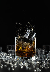 A splash of whiskey and a falling ice cube in a glass on a black background among crushed ice similar to diamonds