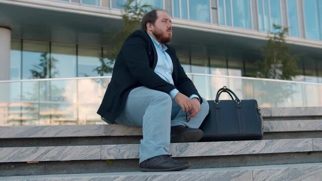 Overweight sad businessman sitting on stairs outdoor lost business. Realtime