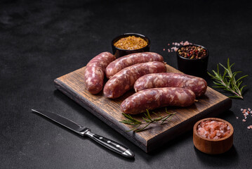 Raw pork sausages grill with spices and herbs on a dark concrete table
