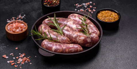 Raw pork sausages grill with spices and herbs on a dark concrete table
