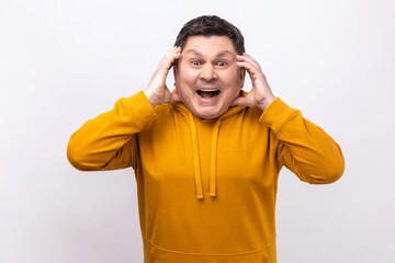 Portrait of amazed shocked middle aged man standing and looking at camera with big eyes, open mouth and touching his face, wearing urban style hoodie. Indoor studio shot isolated on white background.