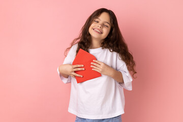 Portrait of satisfied little girl wearing white T-shirt standing open red envelope with...
