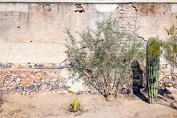 Adobe covers a rock wall in the desert southwest. Cacti are in front of the wall. 