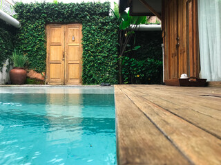 The water pool is surrounded by pots with plants, a floor made of wood and an entrance around which there are vines